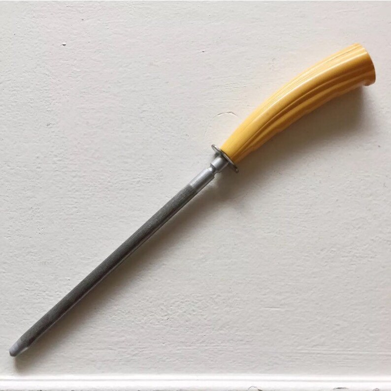 May include: A steel knife sharpener with a yellow plastic handle. The handle has a ribbed design.