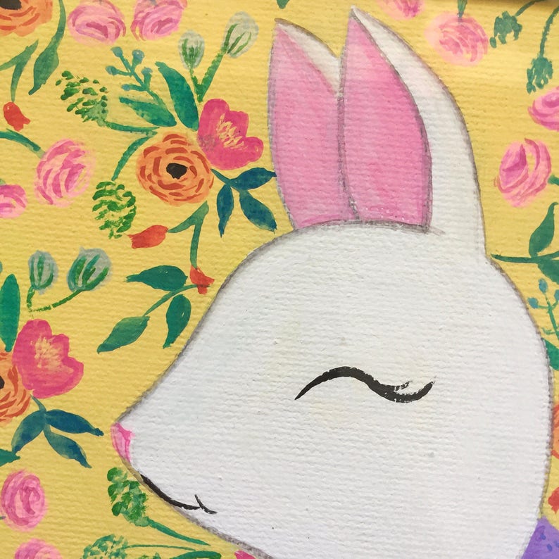 May include: A white bunny with pink ears is painted on a yellow background with a floral pattern. The bunny has a closed eye and a small smile.