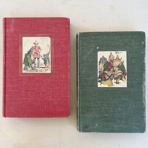 May include: Two vintage hardcover books. One is red with a framed illustration of a man and two figures. The other is green with a framed illustration of two figures in ornate clothing. Both books show signs of wear.
