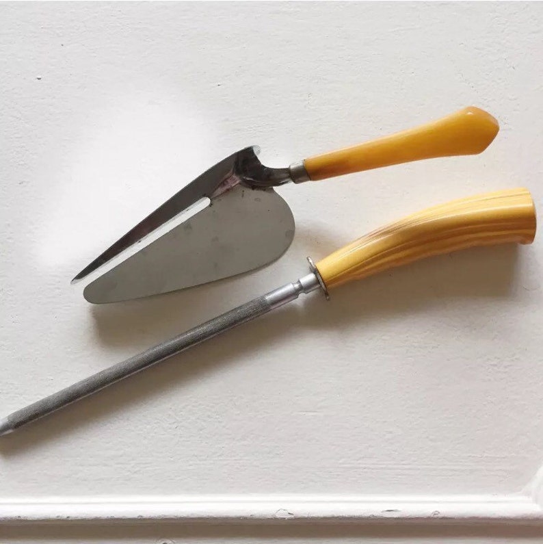 May include: A set of two kitchen tools with yellow plastic handles. The first tool is a silver cake server with a pointed tip. The second tool is a silver knife sharpener.