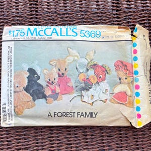 以下が含まれることがあります： 「A Forest Family」と題されたMcCalls 5369のヴィンテージ裁縫型紙封筒。クマ、スカンク、リス、ウサギ、ネズミなどのぬいぐるみが服を着ているイラストが描かれています。テキストには32cmと25cmのサイズが記載されています。