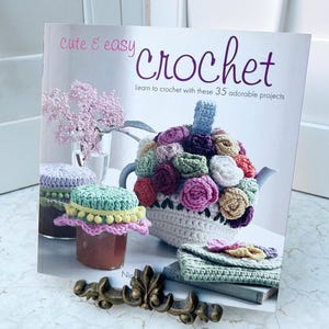 May include: A book titled "Cute & Easy Crochet" with a white background and a colourful crocheted teapot and other crocheted items. The book cover text says "Learn to crochet with these 35 adorable projects."