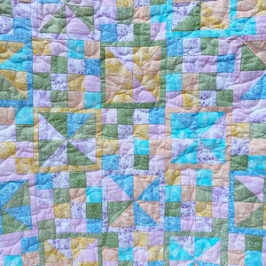 Peut inclure: Une courtepointe faite à la main avec un motif de patchwork composé de carrés et de motifs de roues à broches. La courtepointe présente une variété de couleurs pastel, notamment le bleu, le vert, le jaune et le rose. La courtepointe est en tissu et a une texture matelassée.