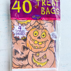 May include: A clear plastic bag containing 40 Halloween treat bags. The purple bag has yellow text that reads "TREAT BAGS" and "40". The treat bags inside feature orange jack-o'-lantern faces. The bag also has a star-shaped sticker that says "4 STYLES INSIDE!"