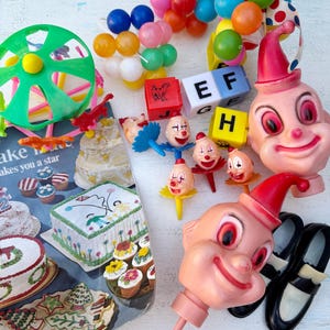 May include: A collection of vintage party decorations and toys, including clown-themed items, colorful balloons, alphabet blocks, and a green pinwheel. The image also features a cake decorating magazine with various cake designs.