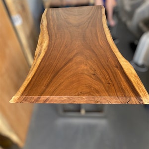 May include: A large, natural wood slab table top with a live edge. The wood is a rich brown color with a beautiful grain pattern. The table top is approximately 30 inches wide and 60 inches long.