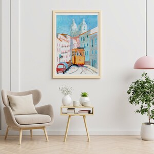 May include: A watercolor painting of a yellow tram traveling up a hill in a city. The tram is surrounded by buildings with white and blue facades. The painting is framed in a light wood frame.