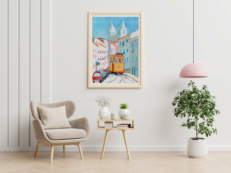 May include: A watercolor painting of a yellow tram traveling up a hill in a city. The tram is surrounded by buildings with white and blue facades. The painting is framed in a light wood frame.