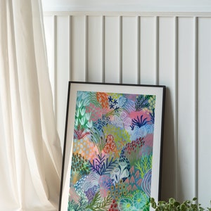 May include: A framed abstract painting with a colorful floral design in shades of pink, blue, green, and red. The painting is set against a white wall with white wainscoting.