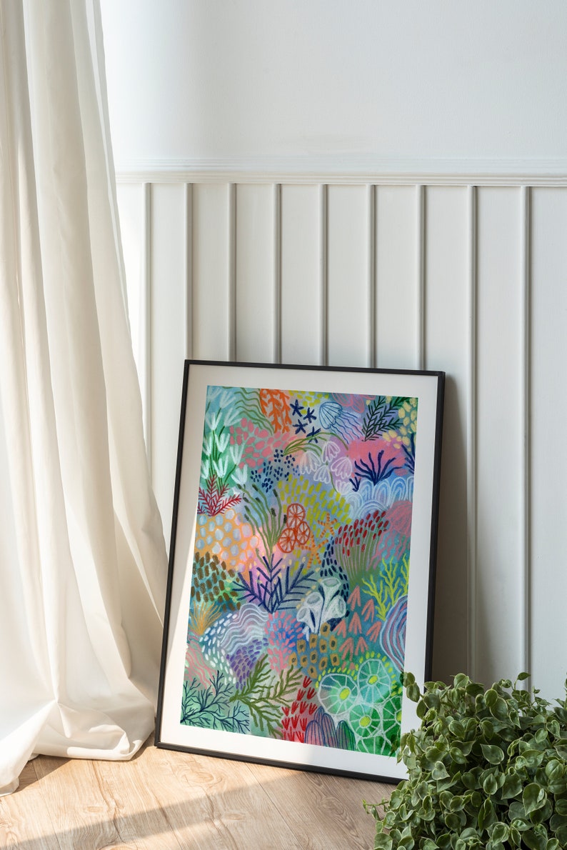 May include: A framed abstract painting with a colorful floral design in shades of pink, blue, green, and red. The painting is set against a white wall with white wainscoting.