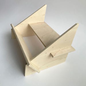 Può includere: Un espositore in legno chiaro con una base rettangolare e due lati inclinati che formano una forma triangolare. L'espositore è progettato per tenere gli articoli in posizione verticale.