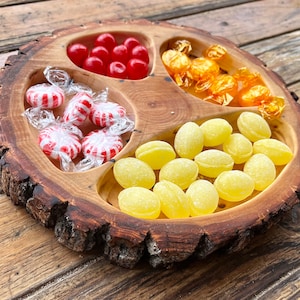 May include: A wooden bowl with three sections, each filled with different sweets. The top section has red and white striped sweets, the middle section has red sweets, and the bottom section has yellow sweets.