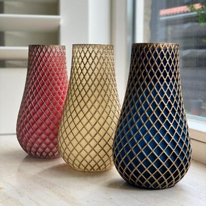 Op de afbeelding: Drie decoratieve vazen met een gouden geometrisch patroon. De vazen zijn peervormig en hebben een textuur. De vazen zijn rood, crème en blauw.
