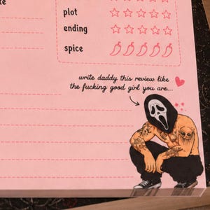 K&ouml;nnte beinhalten: Rosa Notizblock mit Bewertungsskalen f&uuml;r Handlung, Ende und W&uuml;rze, mit Chili-Pfeffer-Symbolen. Es zeigt eine Illustration einer hockenden Figur mit einer Scream-Maske und T&auml;towierungen. Der Text lautet "write daddy this review like the fucking good girl you are..."