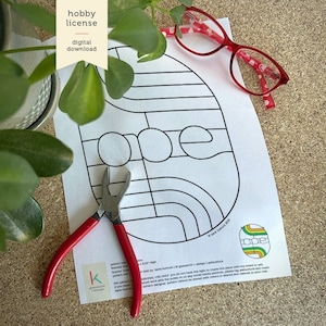 Peut inclure: Une page à colorier imprimable en noir et blanc avec le mot "one" dans un design géométrique. La page est sur une surface brune avec une paire de lunettes rouges et une pince.