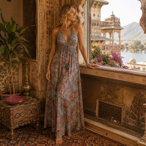 Peut inclure: Une robe longue sans manches avec un décolleté en V profond, une taille à cordon de serrage avec des détails de pompons et un motif cachemire multicolore complexe dans des tons de bleu, rouge et or sur un fond bleu clair.