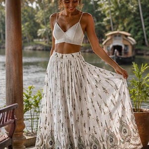 Peut inclure: Un haut court blanc et une longue jupe fluide avec un motif détaillé. La jupe présente un motif répétitif dans les tons de vert et de marron. La tenue est parfaite pour une journée chaude, avec un fond tropical.