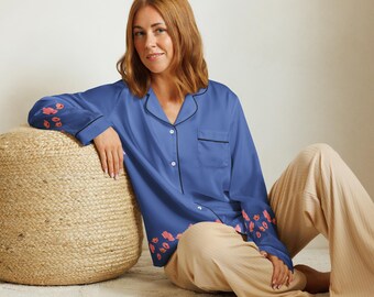 May include: A blue satin pyjama top with black trim and pink floral embroidery. The top has a button-up front and a chest pocket.