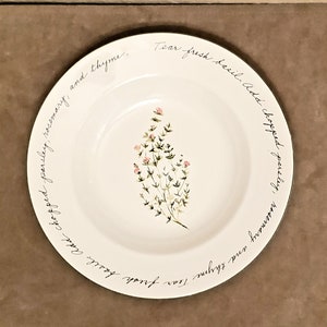 Może przedstawiać: Biała ceramiczna miska z zielonym i różowym wzorem kwiatowym i tekstem "Tear fresh basil. Add chopped parsley, rosemary, and thyme." wokół krawędzi.