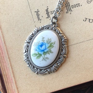 May include: A silver chain necklace with a silver oval pendant featuring a blue and white porcelain rose.