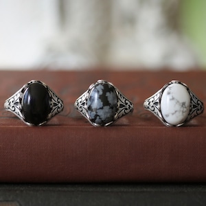 Puede incluir: Tres anillos de plata con piedras de forma ovalada. Los anillos tienen un diseño adornado. Las piedras son negras, grises y blancas.