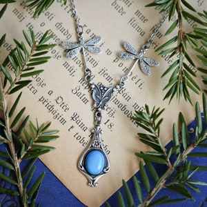 A silver necklace with a blue gemstone pendant and dragonfly charms.
