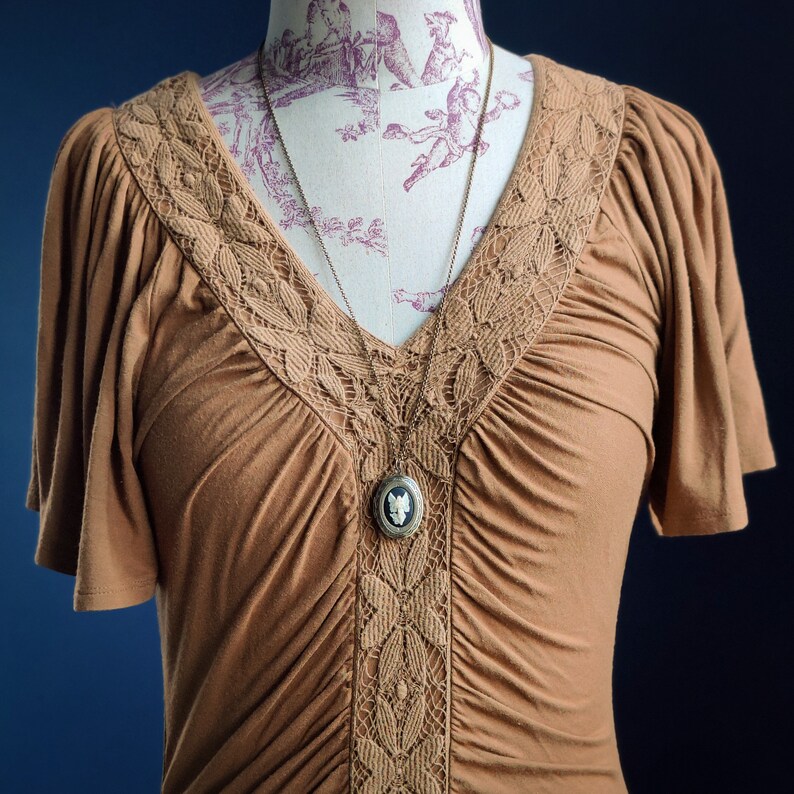 May include: A brown, short-sleeved blouse with a lace trim and a silver chain necklace with a cameo pendant.