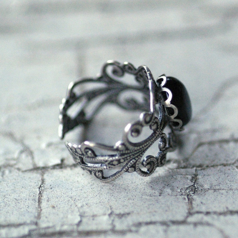 Antiqued silver adjustable filigree ring in vintage-style with a black onyx stone mineral oval cabochon set in a bezel mounted on the front. Rear view.