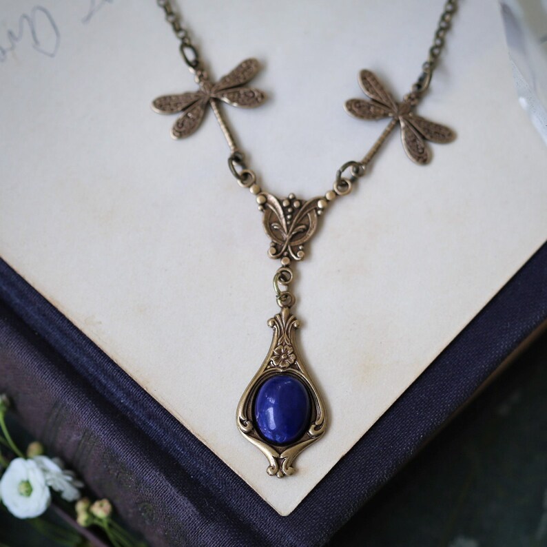 May include: A gold necklace with a blue gemstone pendant and dragonfly accents.