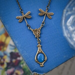 A blue and bronze necklace with a teardrop pendant featuring a blue agate stone and dragonfly accents.