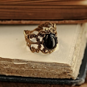 May include: A gold filigree ring with a black gemstone. The ring is on a vintage book.