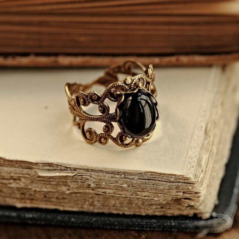 May include: A gold filigree ring with a black gemstone. The ring is on a vintage book.