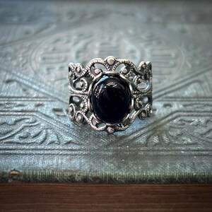 May include: A silver ring with an intricate filigree design and a black gemstone in the center.