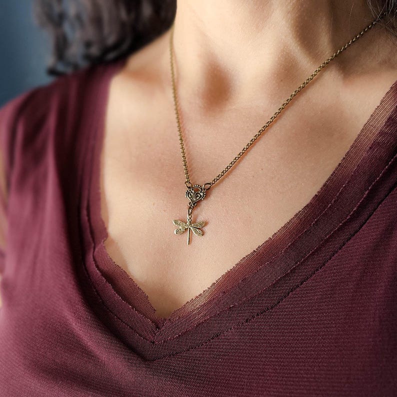 Antiqued brass filigree small dragonfly necklace in vintage syle on a chain with a connector modeled at 18 inches.