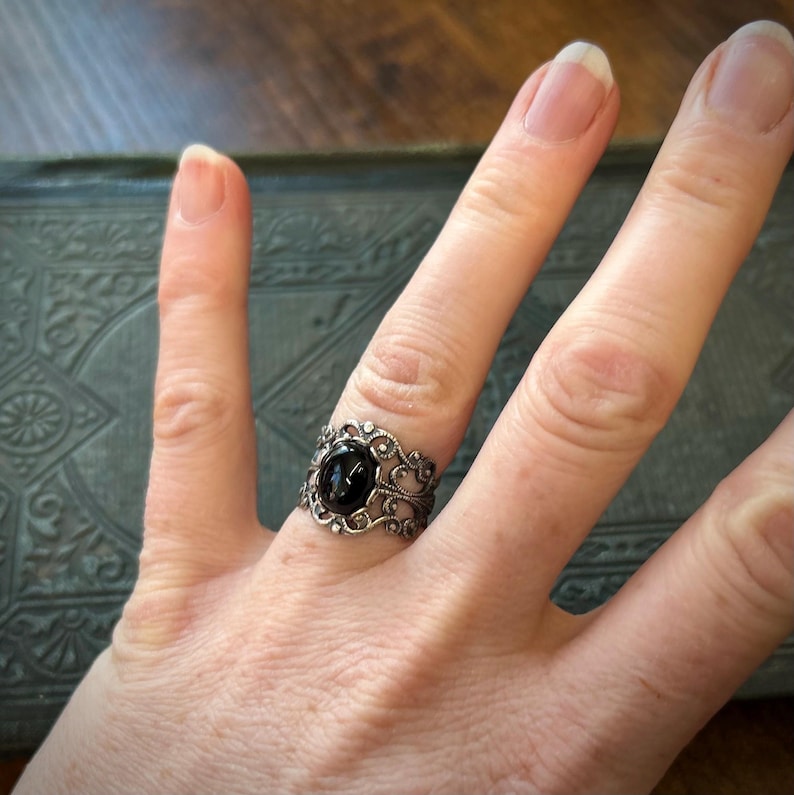 May include: A silver ring with a black gemstone set in a filigree design.