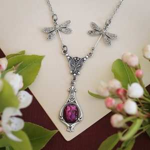 May include: A silver necklace with a pink iridescent stone pendant and two dragonfly charms.