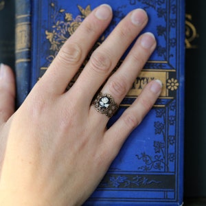 Antiqued brass adjustable filigree ring in vintage-style with a black and white single rose small cameo set in a bezel mounted on the front.