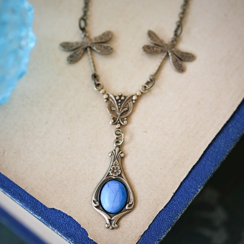 A brass necklace with a blue stone pendant and dragonfly charms.