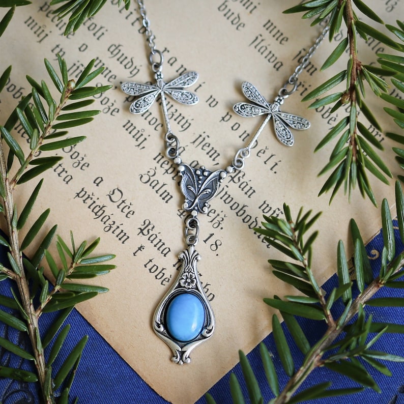 A silver necklace with a blue gemstone pendant and dragonfly charms.