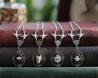 May include: Five silver necklaces with black cameo pendants featuring a dragonfly, angel, thistle, and bee. Each necklace has a pair of silver birds flying above the pendant.