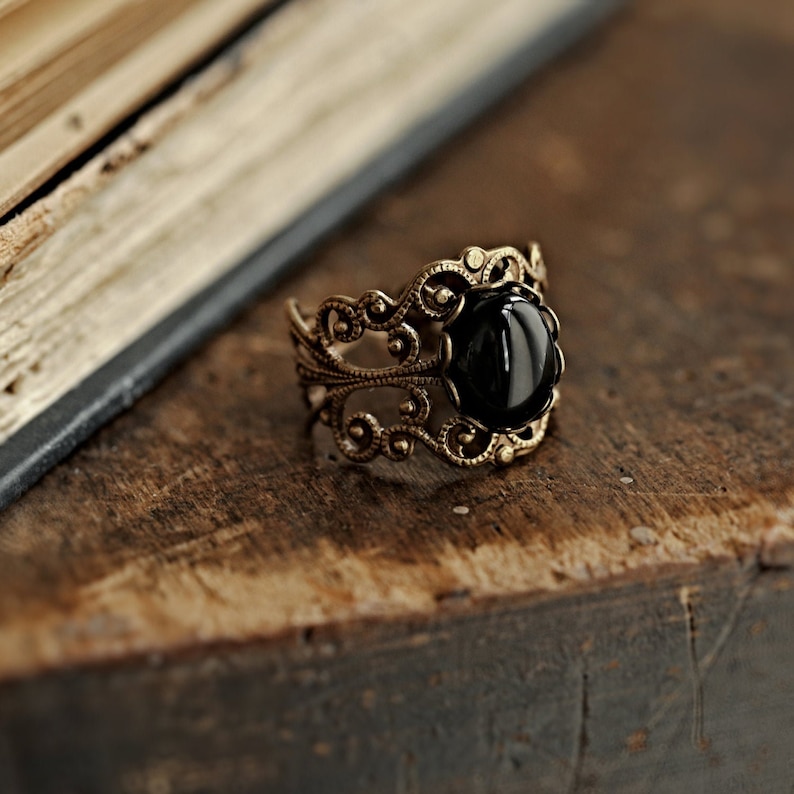 May include: A gold filigree ring with a black gemstone. The ring is on a wooden surface.