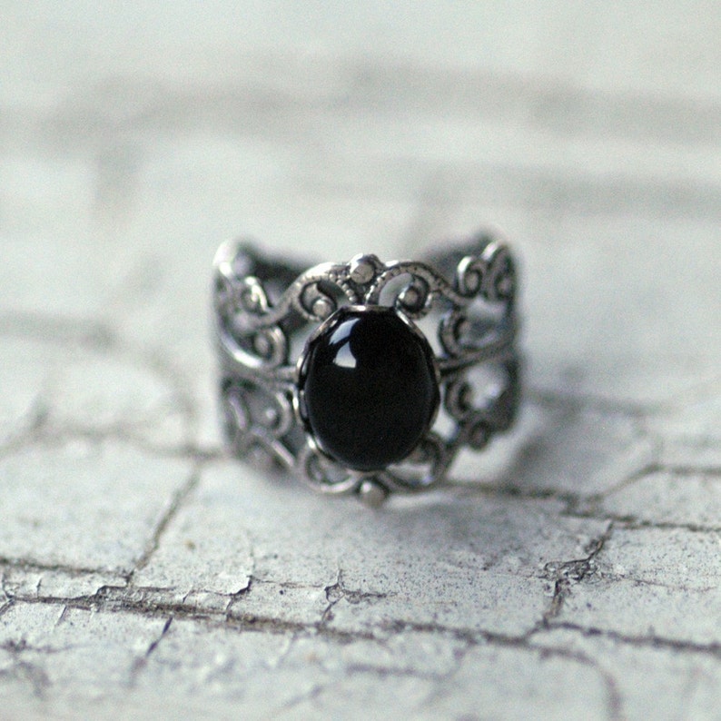 Antiqued silver adjustable filigree ring in vintage-style with a black onyx stone mineral oval cabochon set in a bezel mounted on the front.