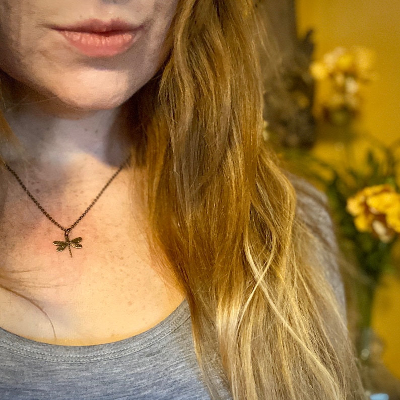 Antiqued brass filigree small dragonfly necklace in vintage syle on a simple chain modeled at 16 inches.