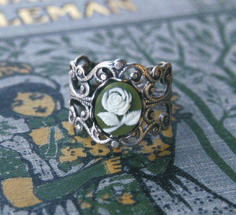 Green and white small rose cameo set in a bezel on an antiqued silver adjustable filigree ring in vintage-style.