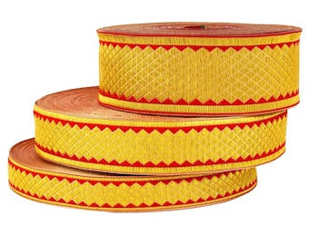 Op de afbeelding: Drie rollen decoratief lint. Het lint is goudkleurig met een rood geometrisch patroon langs de randen. De rollen zijn op elkaar gestapeld, waarbij het ontwerp wordt getoond. Elke rol is ongeveer 5 cm hoog.