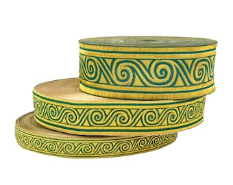 May include: Three spools of decorative ribbon stacked on top of each other. The ribbon has a gold base with a green, embroidered, repeating swirl pattern. The spools are of varying sizes, with the largest spool on top.