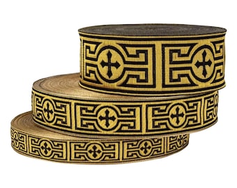 May include: Three rolls of decorative ribbon with a repeating geometric pattern in black and gold. The ribbon features a cross design within a square and rectangular border. The rolls are stacked on top of each other.