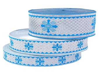 May include: Three spools of decorative ribbon. The ribbon is silver with a blue geometric pattern. The spools are stacked on top of each other. The top of the spools are blue.