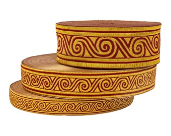 May include: Three spools of decorative ribbon. The ribbon has a gold background with a repeating burgundy swirl pattern. The edges are trimmed with a gold fringe. The spools are stacked on top of each other.
