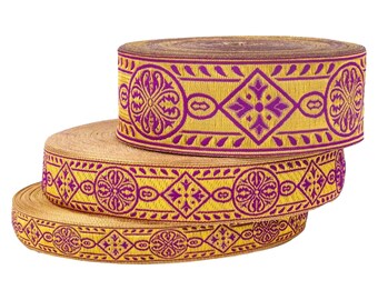 May include: Three spools of decorative ribbon. The ribbon has a gold background with a repeating purple geometric pattern. The pattern includes diamond and circular shapes. The spools are stacked on top of each other.